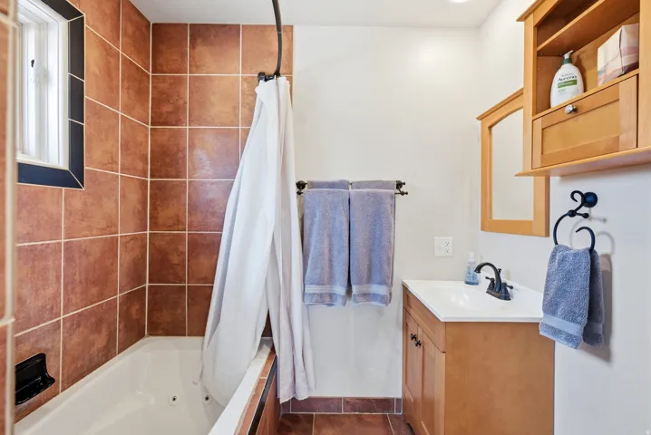 Bathroom featuring a built-in tub with tile surround, a single vanity with storage, and a wall-mounted medicine cabinet