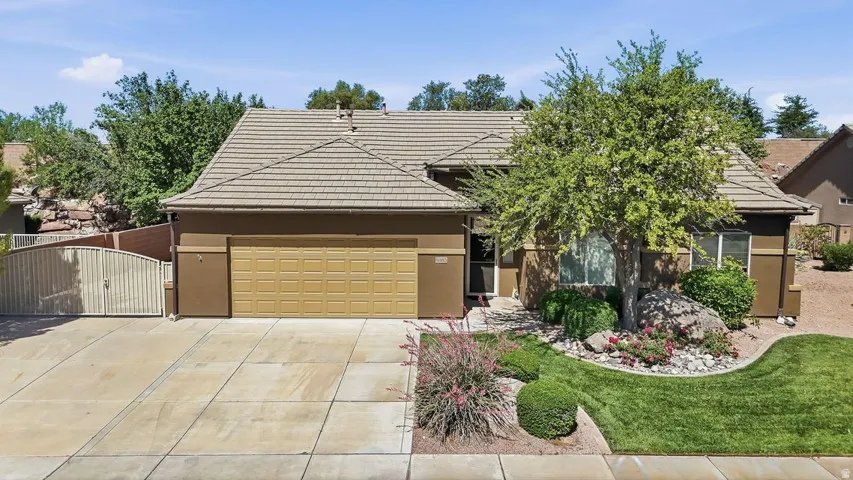 Single-story exterior featuring a tile roof, an integrated garage with a sectional door, a concrete driveway, a privacy gate, and mature front landscaping with turf and decorative rock