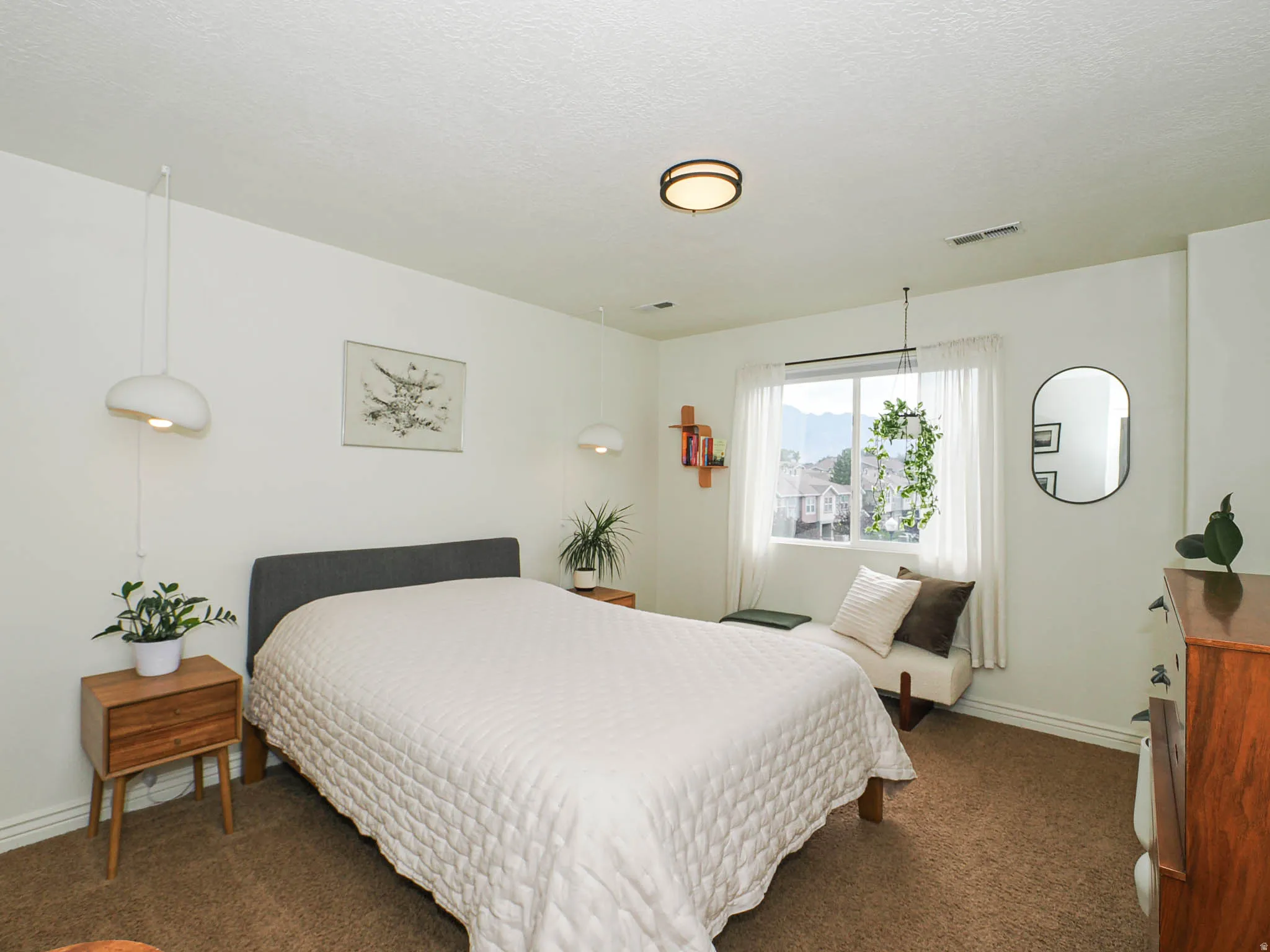 Bright bedroom featuring a large window, neutral carpeting, and a modern ceiling light fixture