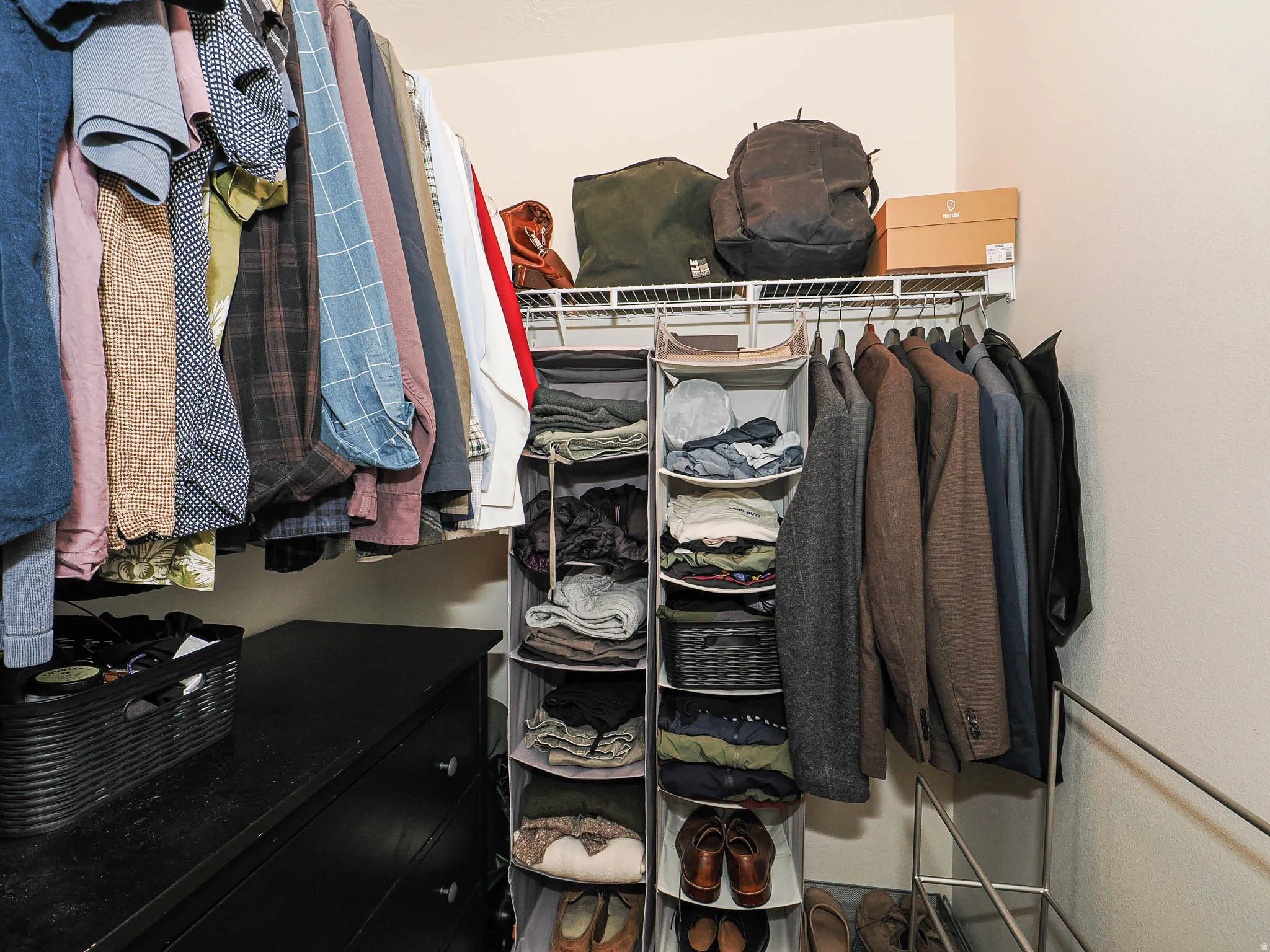Wardrobe space featuring white wire shelving, a black dresser, and neutral wall tones