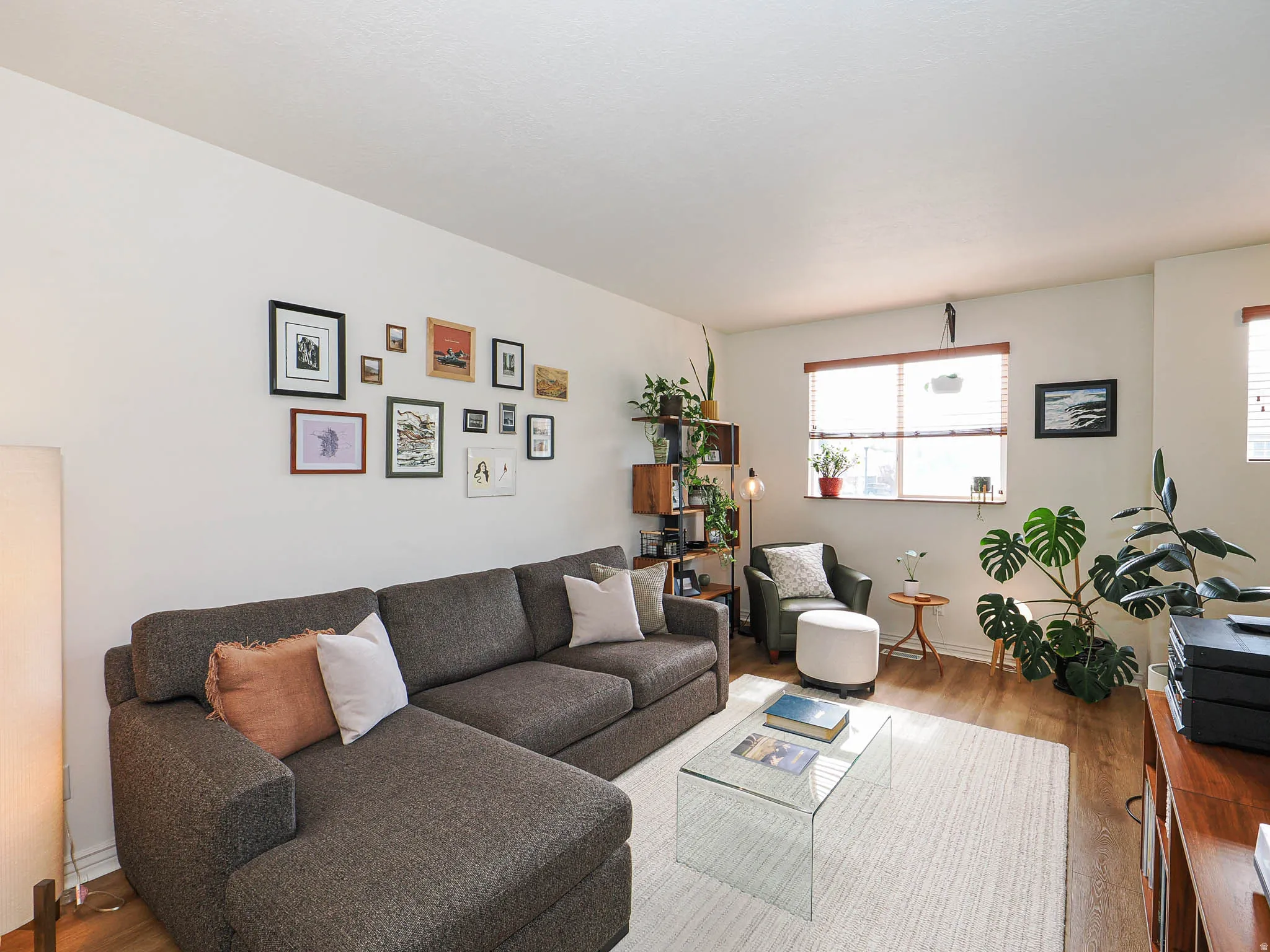 Spacious living area featuring light-toned walls, wood-finish flooring, and a large window with blinds