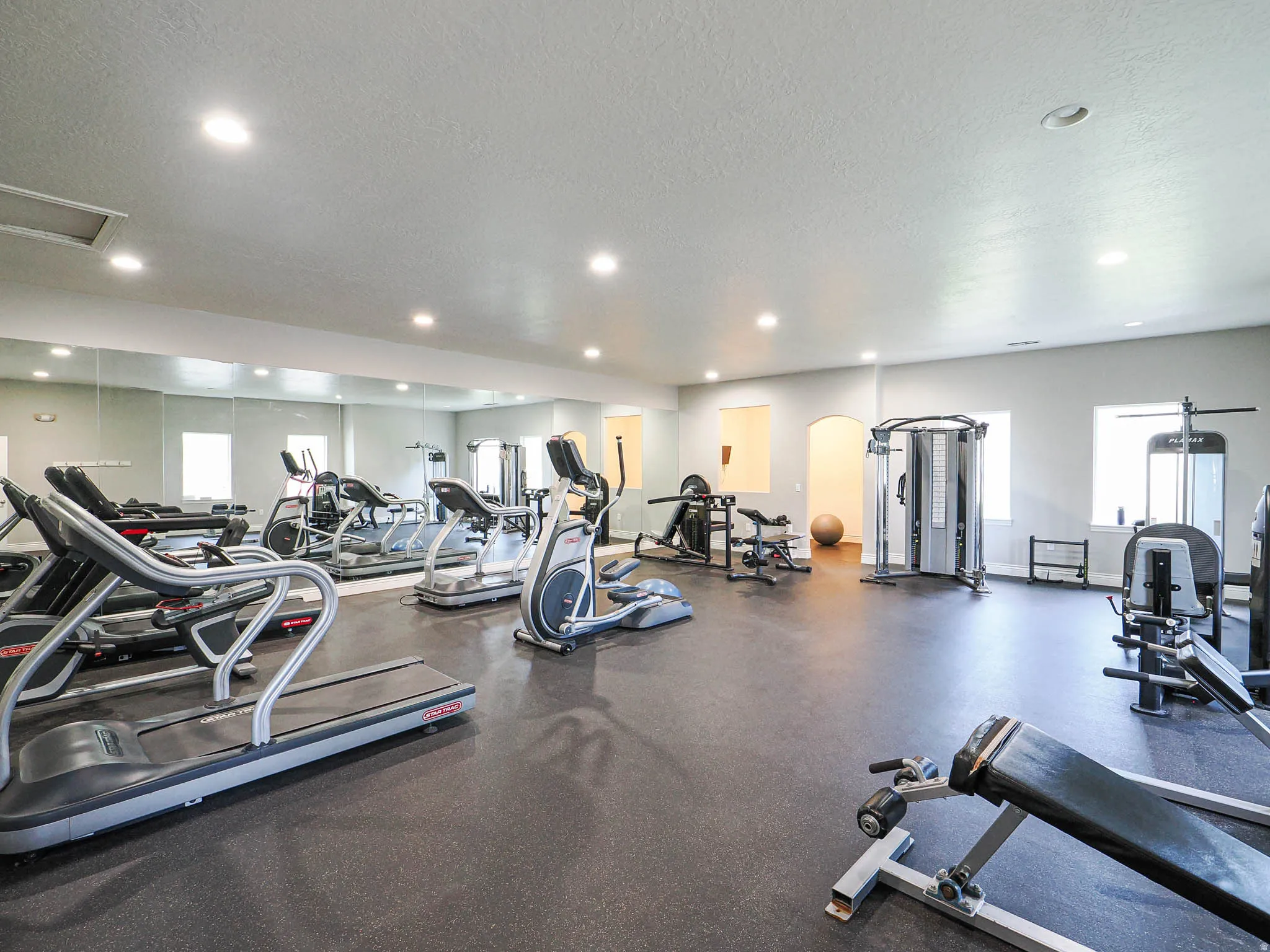 Dedicated fitness area featuring rubberized flooring, multiple cardio machines, weight training equipment, and mirrored walls