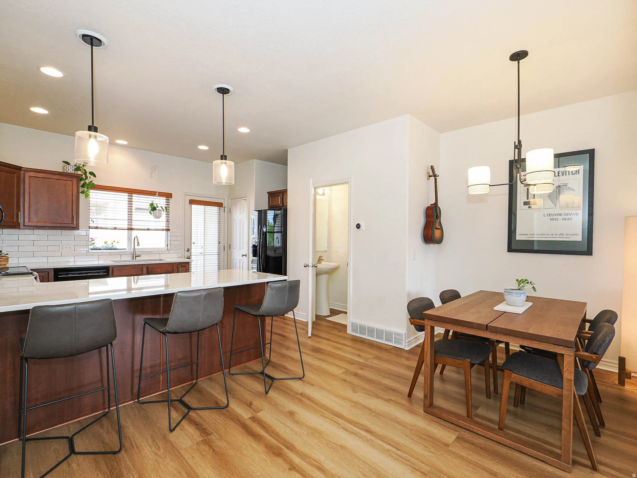 Open-concept kitchen and dining area featuring wood-finish flooring, a kitchen island with seating, dark wood cabinetry, a subway tile backsplash, and recessed lighting