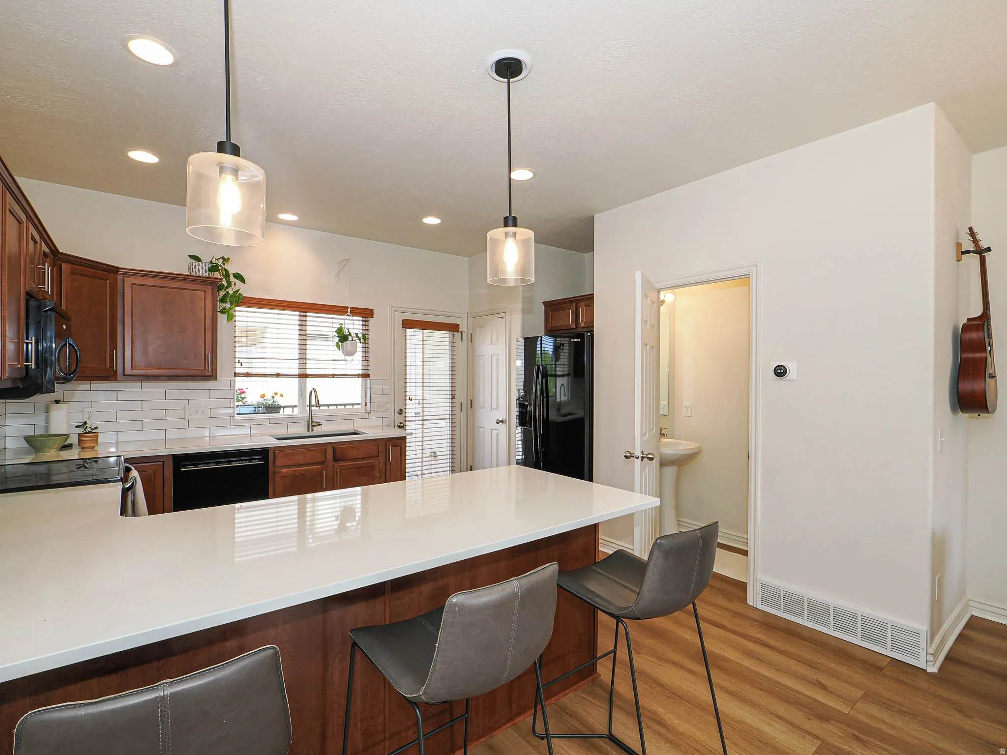 Kitchen featuring a large central island with a light-toned countertop, pendant lighting, wood-finish flooring, dark wood cabinetry, and a subway tile backsplash