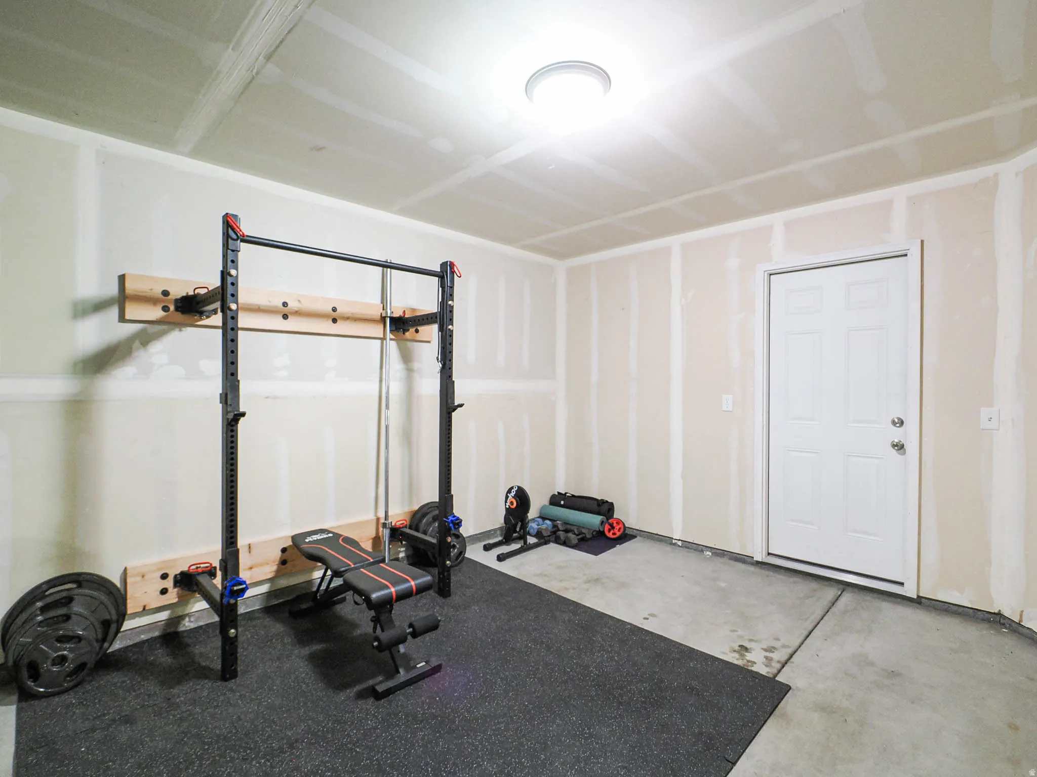 Garage space featuring exposed drywall, a concrete floor, and a white entry door