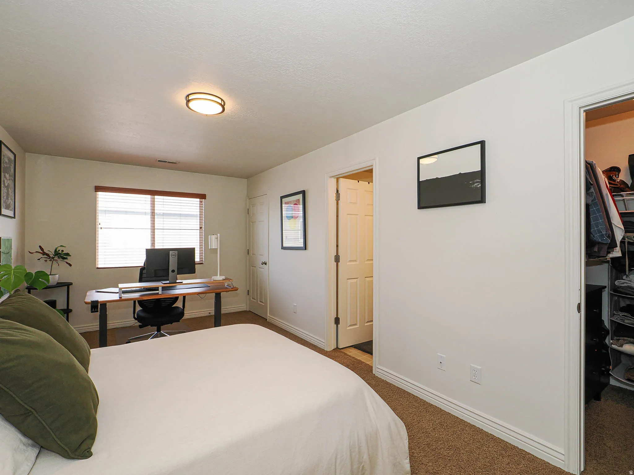 Spacious room featuring neutral carpeting, a built-in closet with shelving, a window with horizontal blinds, and a flush-mount ceiling light