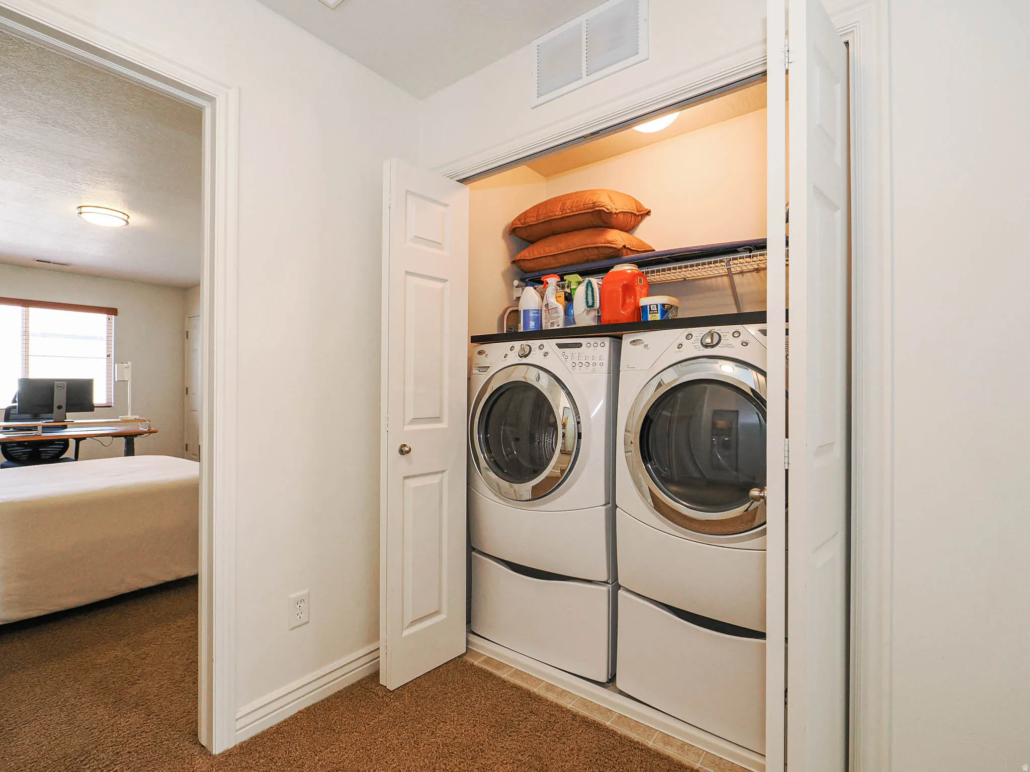 Dedicated laundry closet featuring a stacked washer and dryer with storage shelf