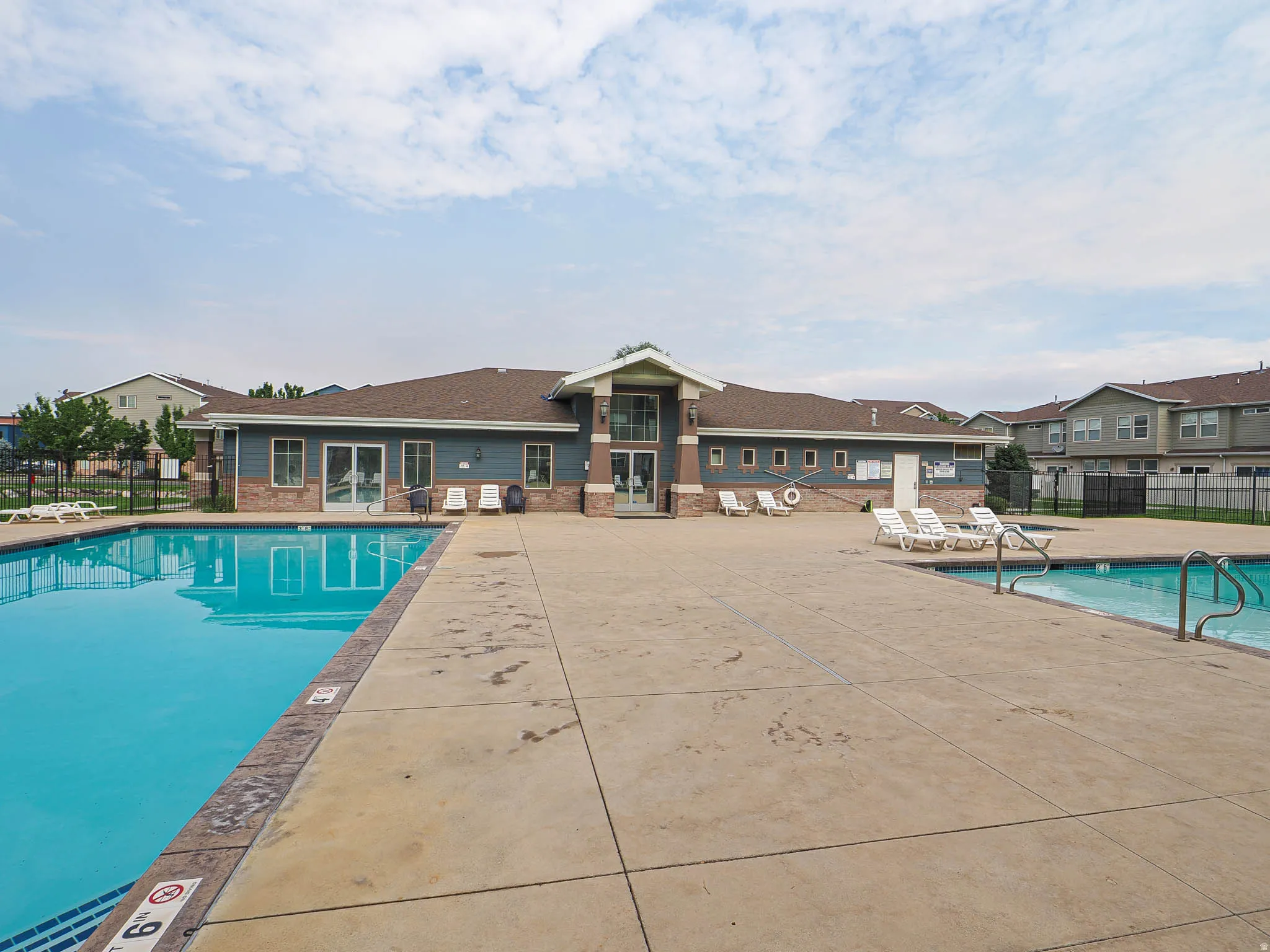 Community swimming pool with an expansive concrete deck, surrounded by a black metal fence