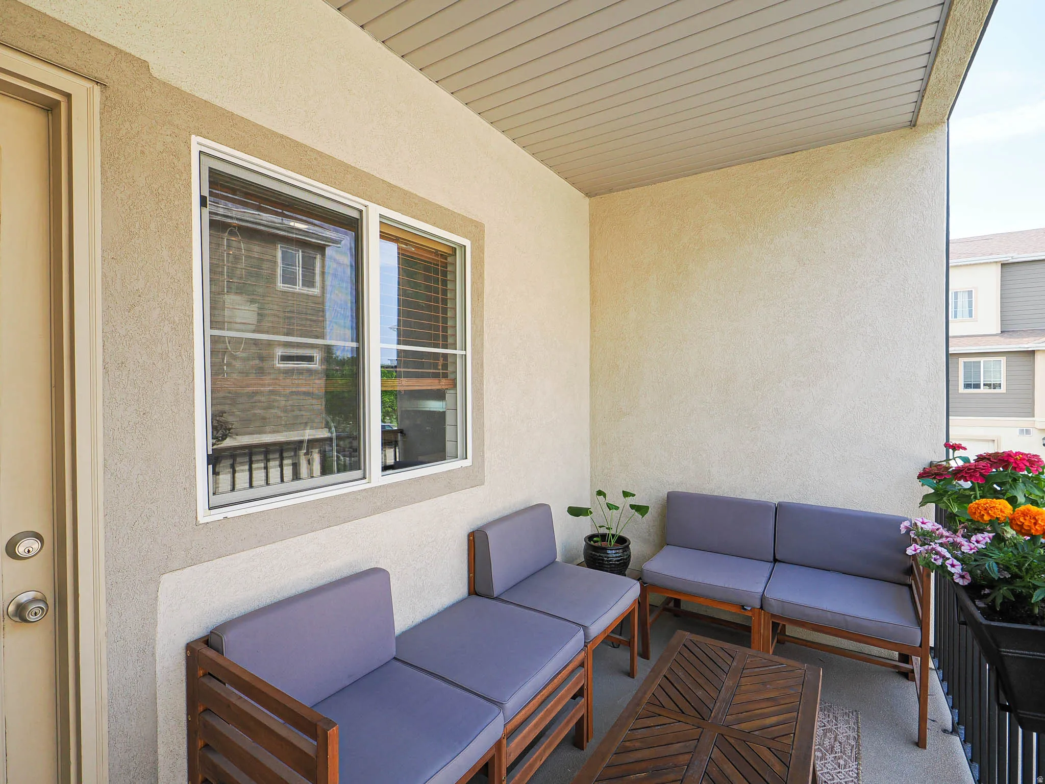 Covered patio featuring a stucco exterior, white-framed windows with blinds, and a durable exterior door