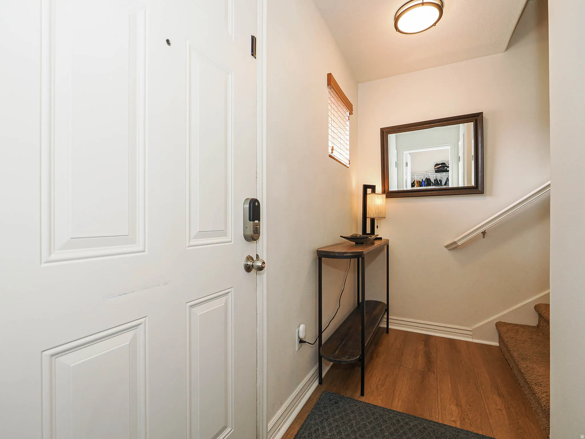 Entryway featuring wood-finish flooring, a contemporary flush-mount ceiling light, a white paneled door with a smart lock, and a staircase with a white handrail