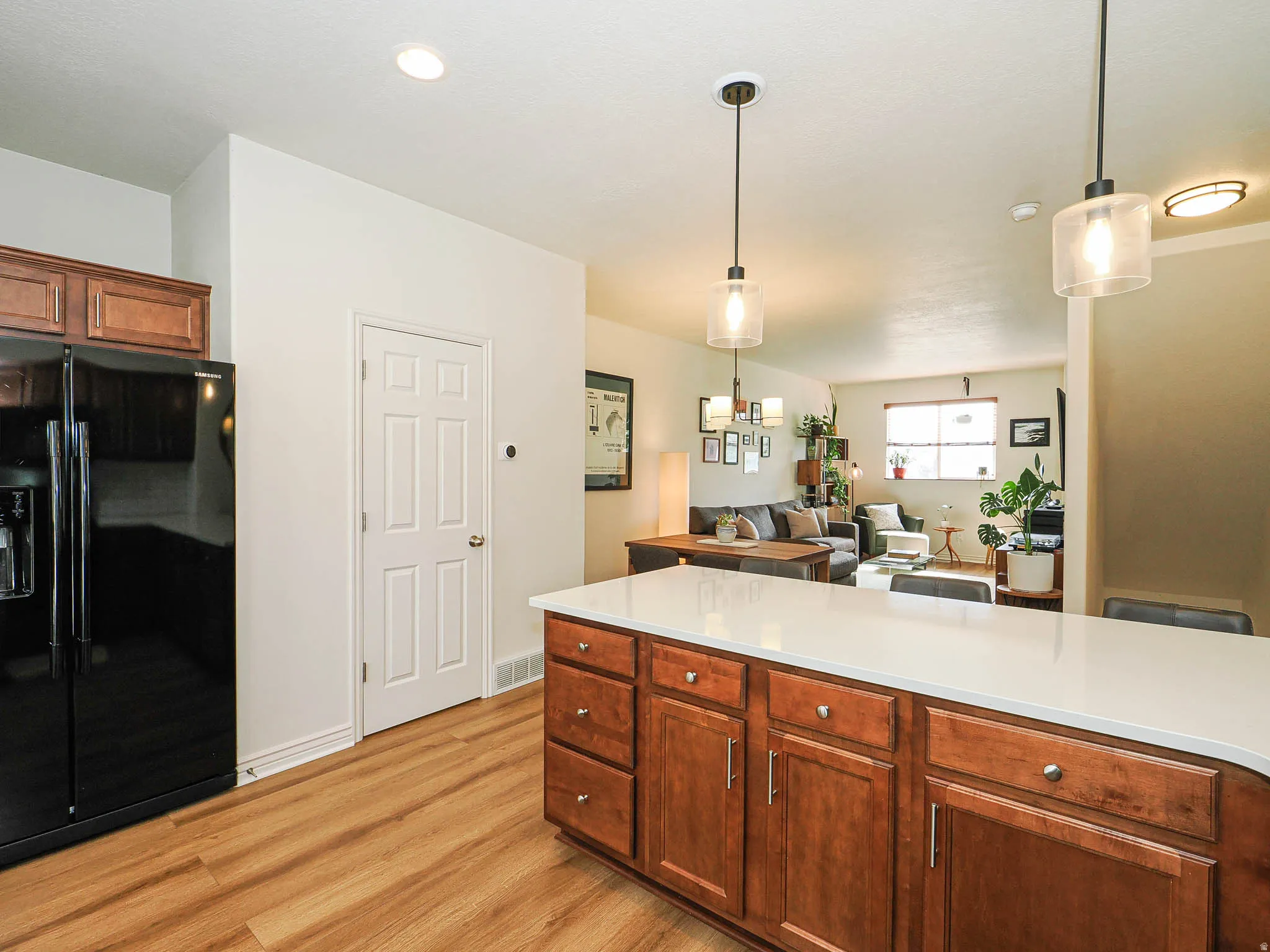 Kitchen island with wood cabinetry, light-toned countertop, and two pendant light fixtures