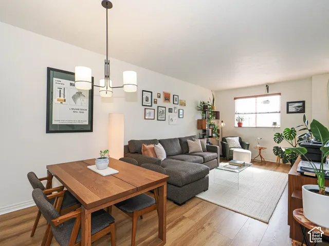 Open-concept living area featuring wood-finish flooring, a contemporary chandelier, and a large window with blinds