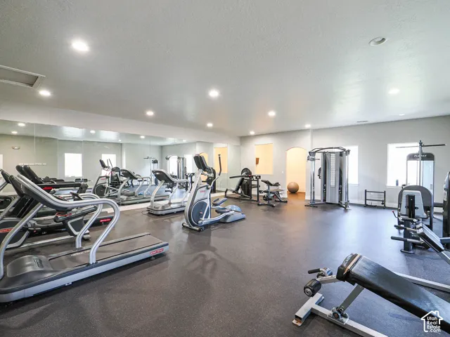 Dedicated fitness area featuring rubberized flooring, multiple cardio machines, weight training equipment, and mirrored walls