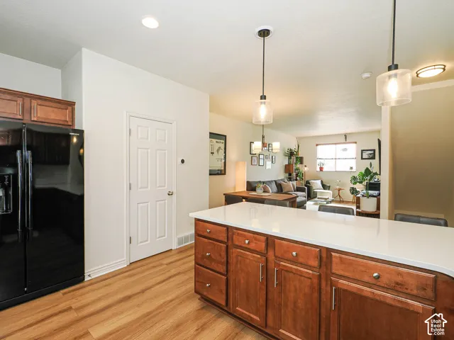 Kitchen island with wood cabinetry, light-toned countertop, and two pendant light fixtures