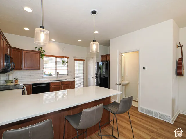 Kitchen featuring a large central island with a light-toned countertop, pendant lighting, wood-finish flooring, dark wood cabinetry, and a subway tile backsplash