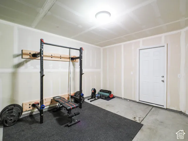 Garage space featuring exposed drywall, a concrete floor, and a white entry door