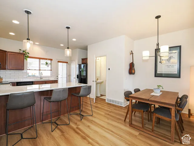 Open-concept kitchen and dining area featuring wood-finish flooring, a kitchen island with seating, dark wood cabinetry, a subway tile backsplash, and recessed lighting