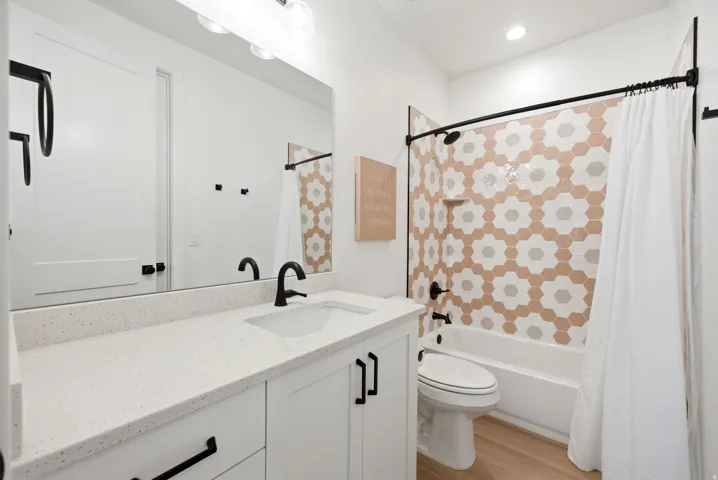 Bathroom featuring a white vanity with a light-toned countertop, matte black fixtures, wood-finish flooring, a full-width mirror, and a tub/shower combination with decorative hexagonal tiling