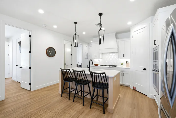 Contemporary kitchen featuring a light wood-finish island with seating for three, white cabinetry, integrated stainless steel appliances, and a diagonal patterned tile backsplash