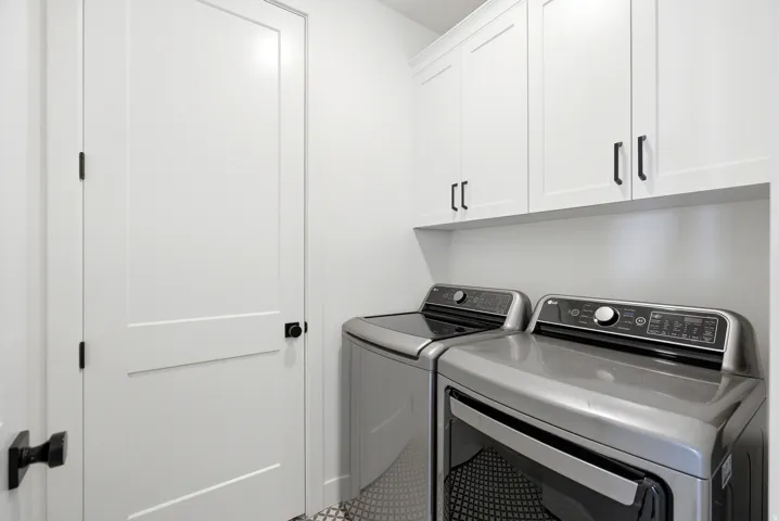 Dedicated laundry area featuring white shaker-style cabinetry with matte black hardware
