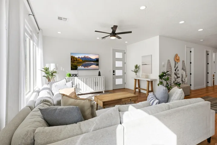 Spacious living area featuring large windows, recessed lighting, wood-finish flooring, a contemporary ceiling fan, and a four-panel frosted glass entry door