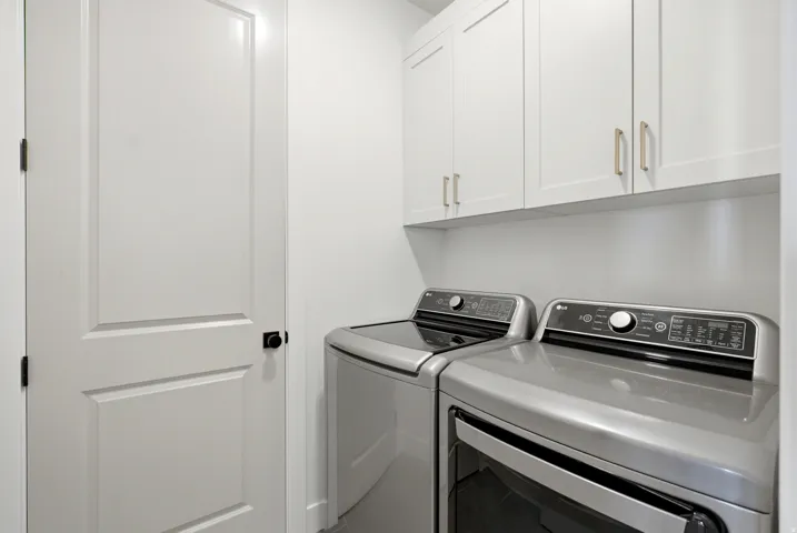 Dedicated laundry area featuring white shaker-style cabinetry with gold-tone hardware, providing overhead storage