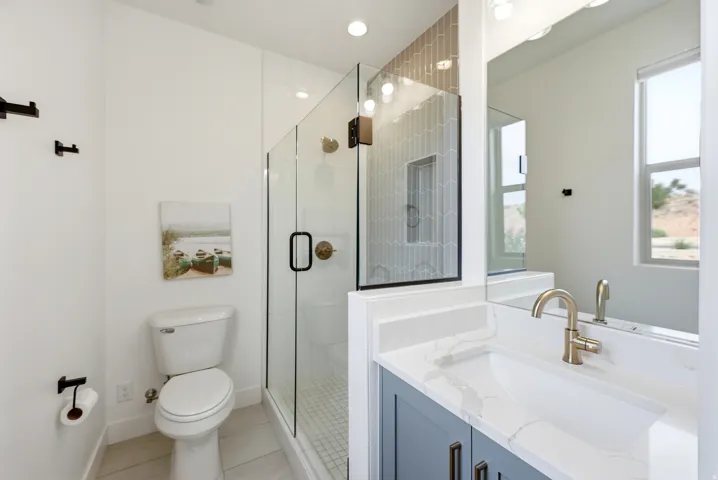 Bathroom featuring a frameless glass shower enclosure with hex tile surround and built-in niche, a single vanity with a quartz countertop, integrated sink, and brushed brass faucet, and wood-finish flooring
