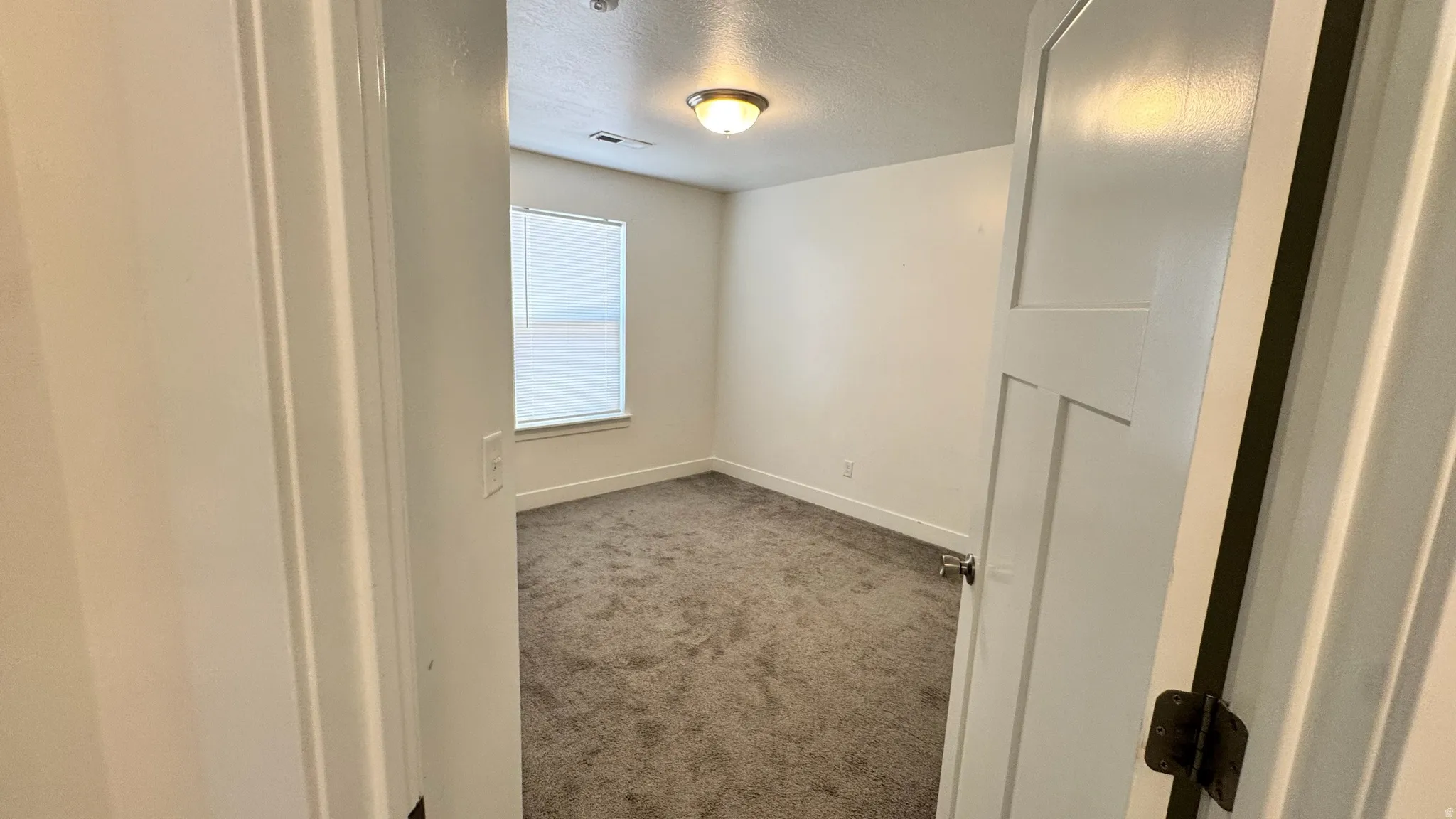 Room featuring textured carpet flooring, white painted walls, and a window with horizontal blinds