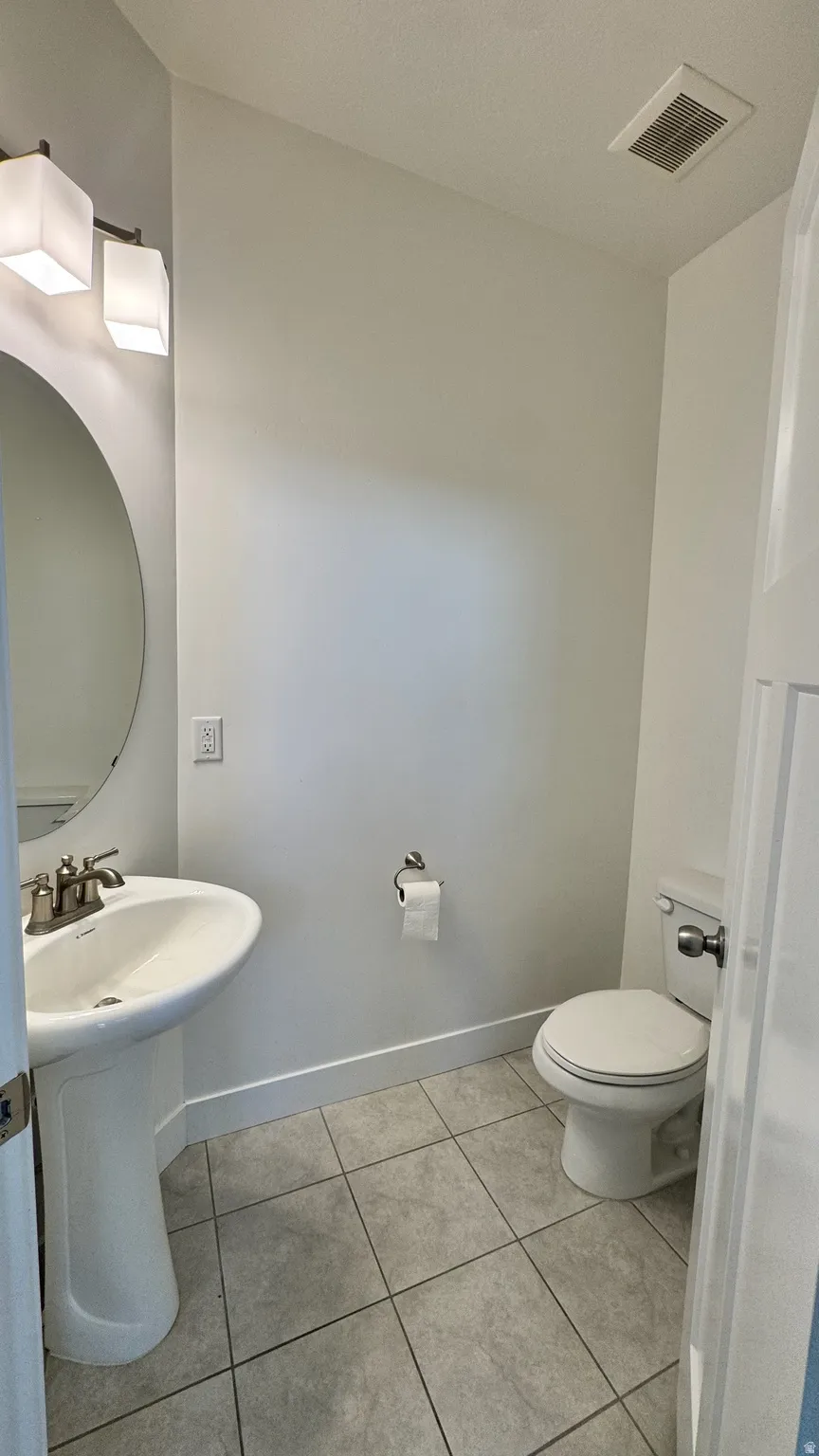 Bathroom featuring a pedestal sink with brushed nickel faucet, an oval wall-mounted mirror, and tile flooring