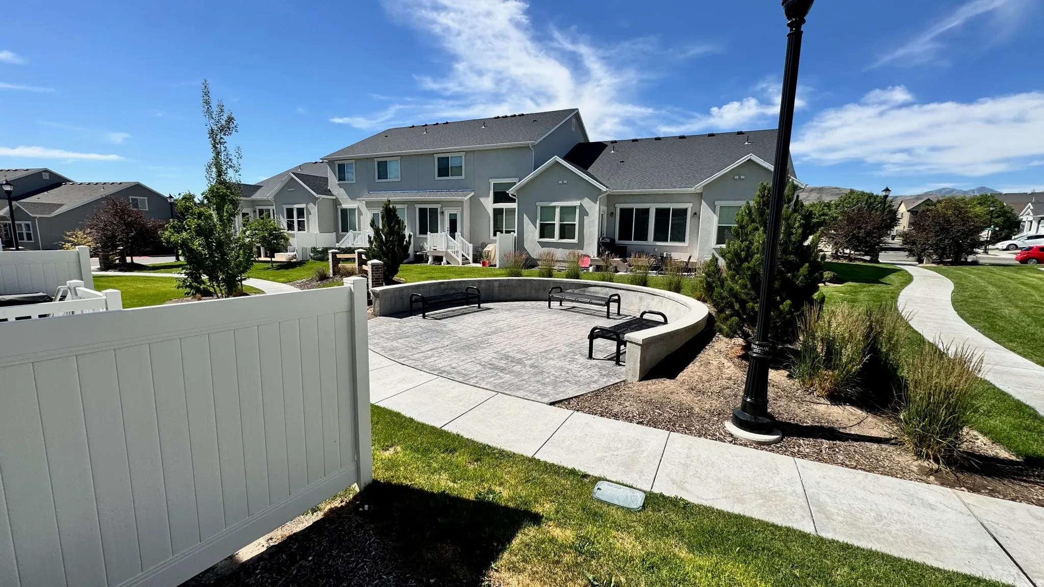 Community green space featuring a curved concrete patio with seating, bordered by landscaping and a paved walkway