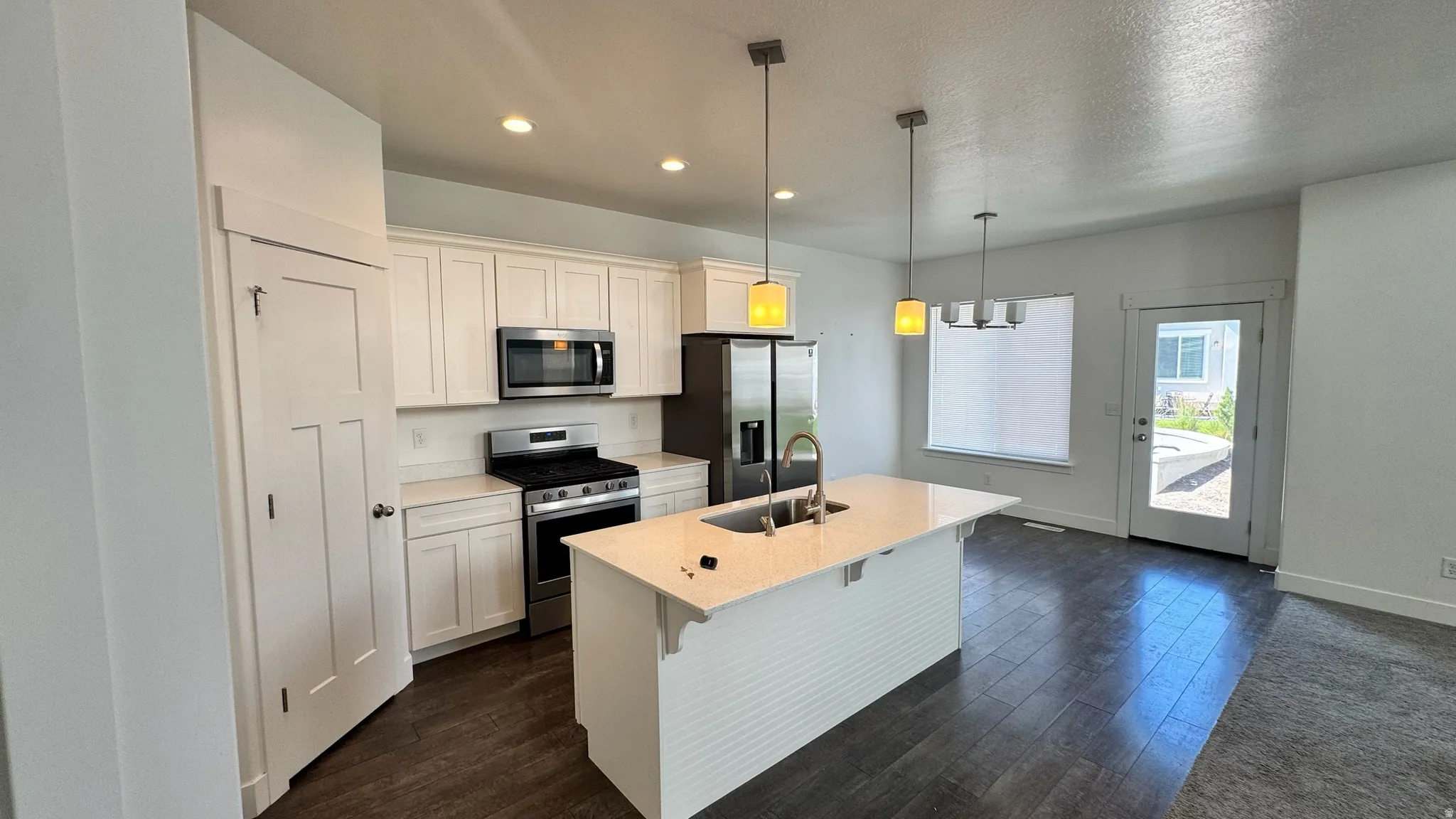 Modern kitchen featuring white shaker cabinetry, stainless steel appliances, a center island with sink and pendant lighting, wood-finish flooring, and a glass-paneled exterior door