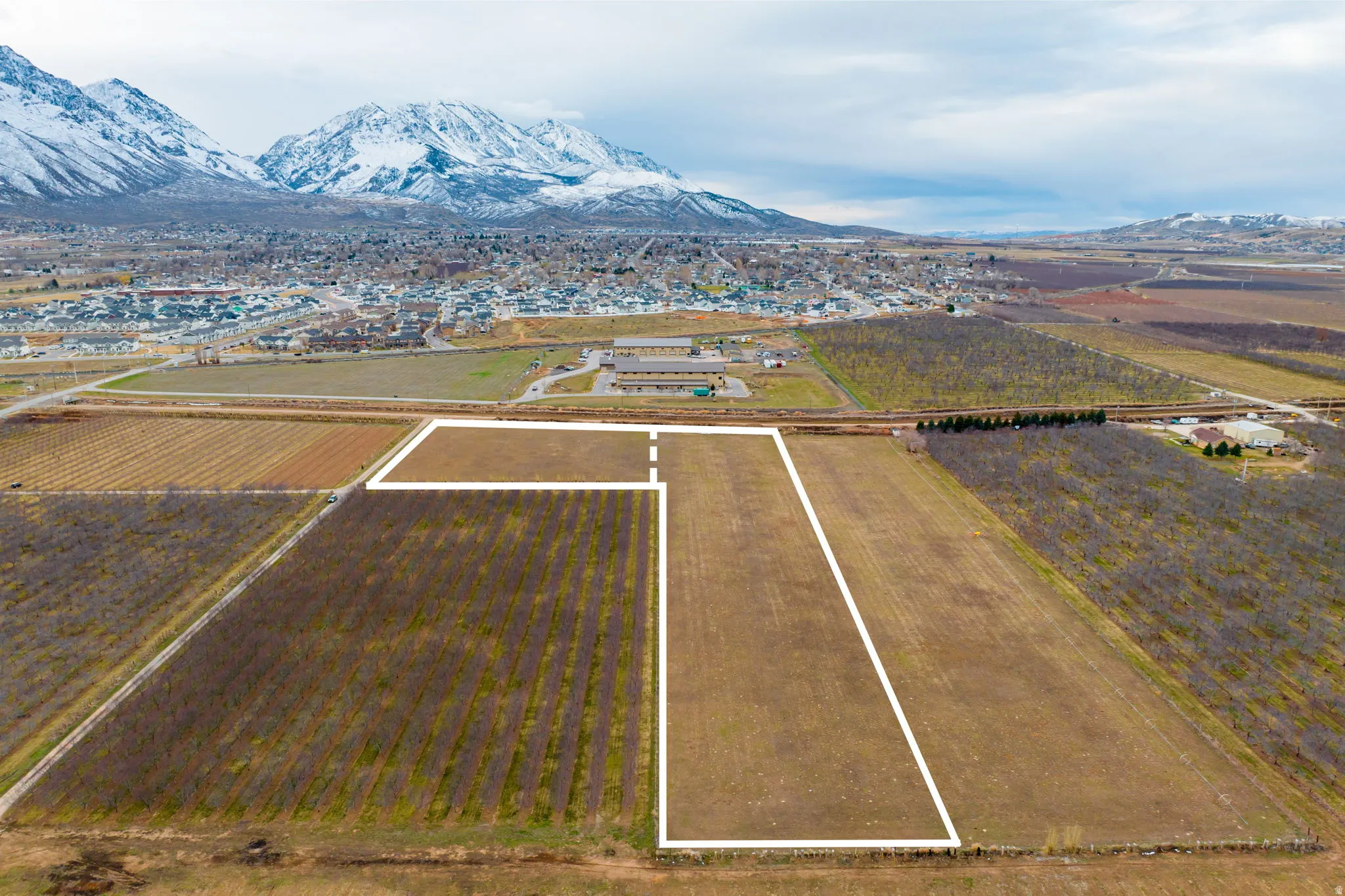 Expansive undeveloped land parcel outlined in white, featuring agricultural fields and distant mountainous terrain