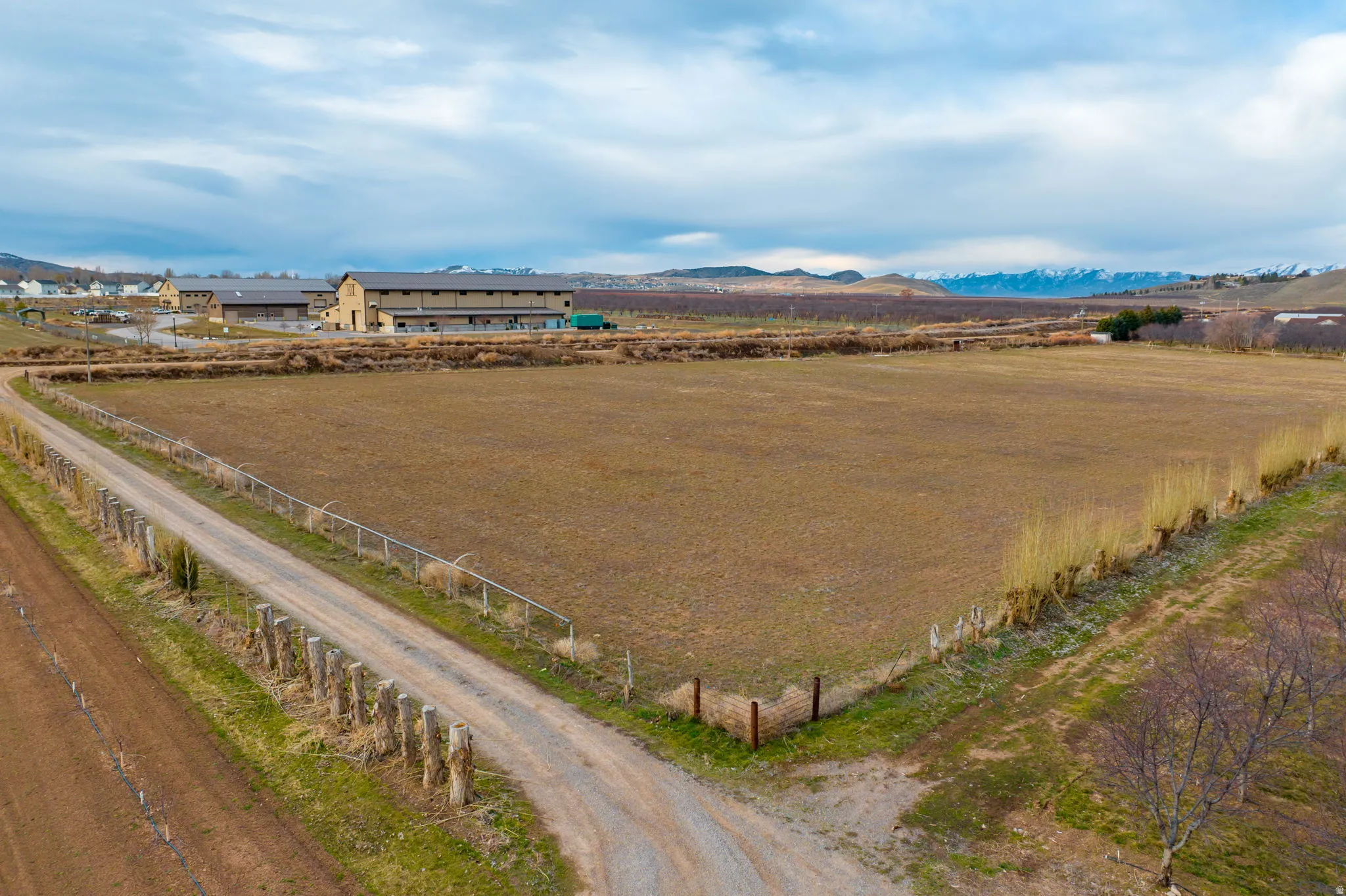 Expansive land parcel featuring a gravel driveway, agricultural fields, distant mountain range, and a large multi-building structure