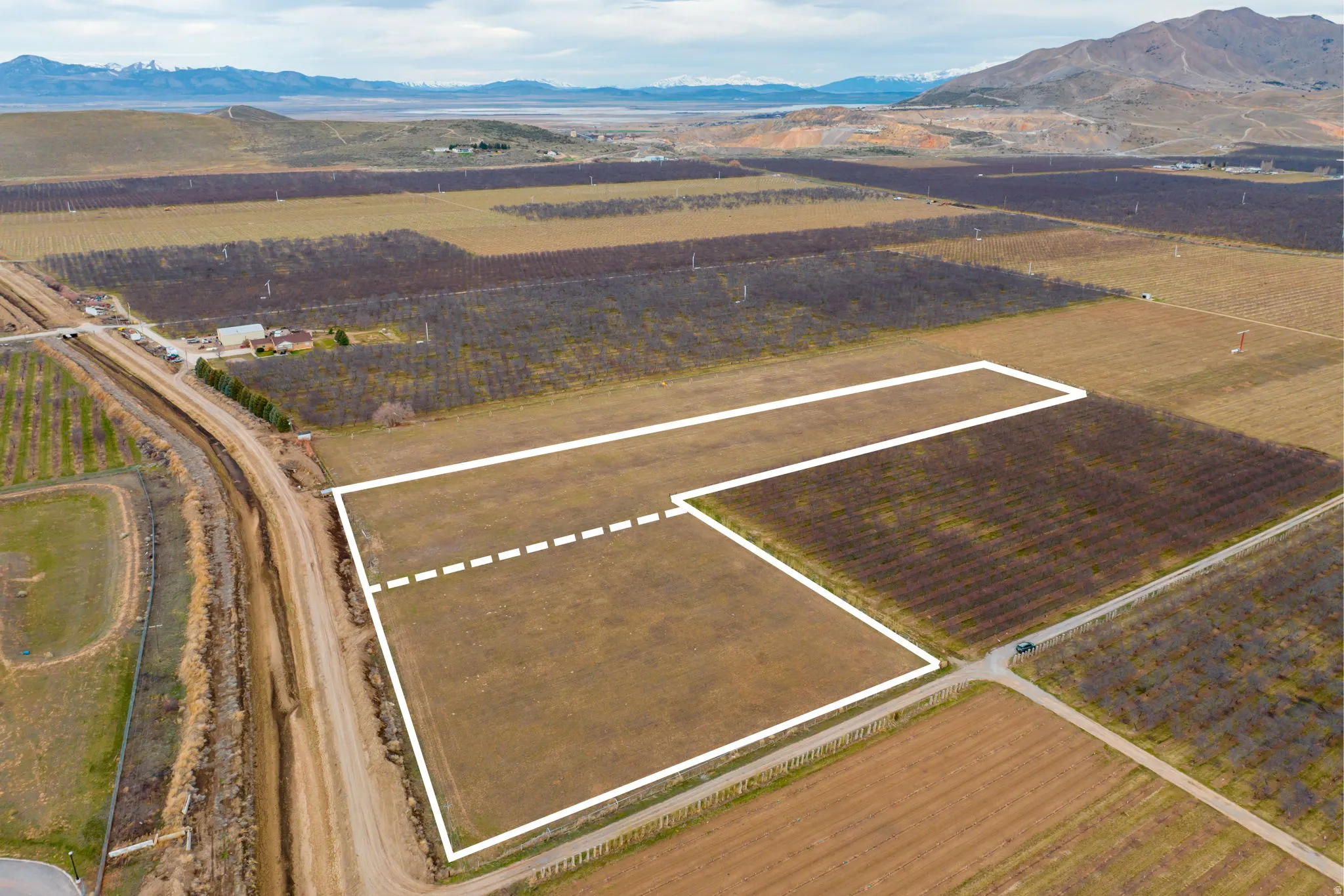 Expansive agricultural land featuring delineated parcels, surrounded by cultivated fields and distant mountains