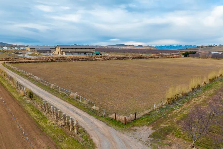 Expansive land parcel featuring a gravel driveway, agricultural fields, distant mountain range, and a large multi-building structure