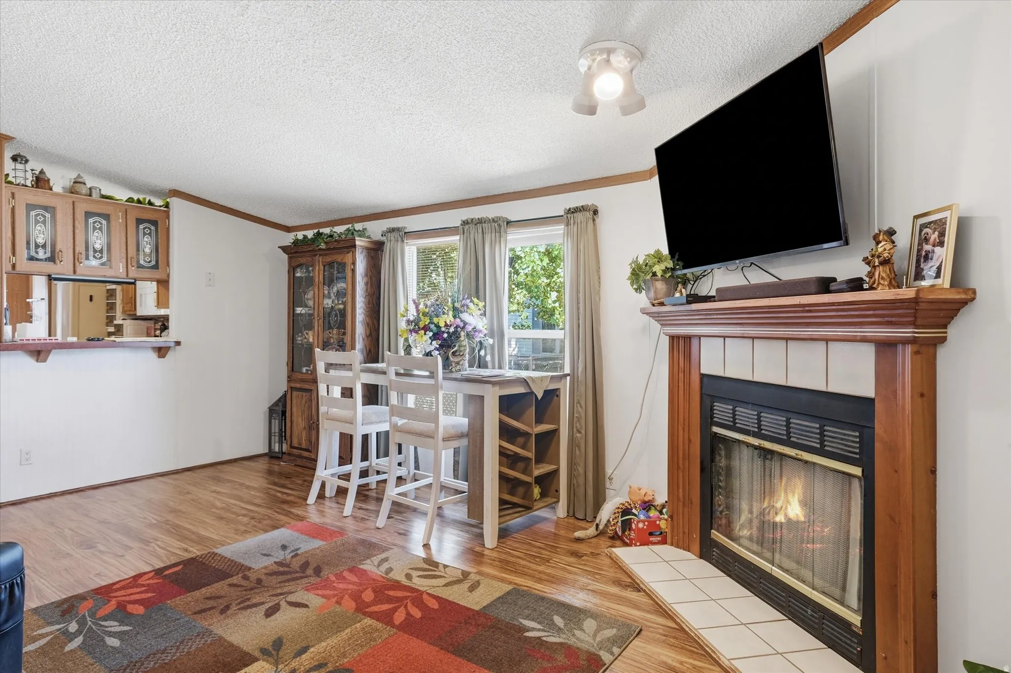 Living area featuring a fireplace with a wood mantle and tile surround, wood-finish flooring, a breakfast bar with built-in cabinetry, and window treatments