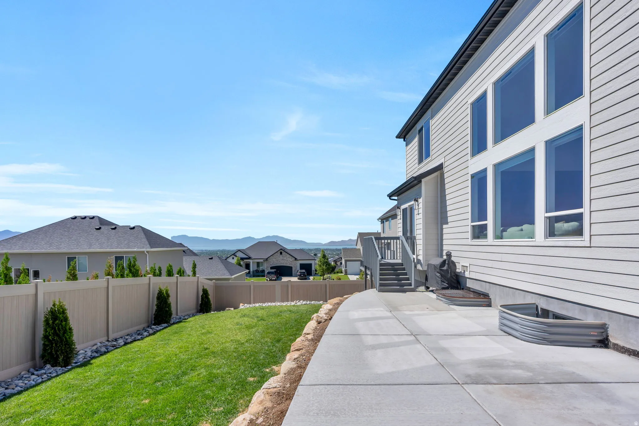 Expansive concrete patio with a graded lawn area, complemented by a light-colored privacy fence