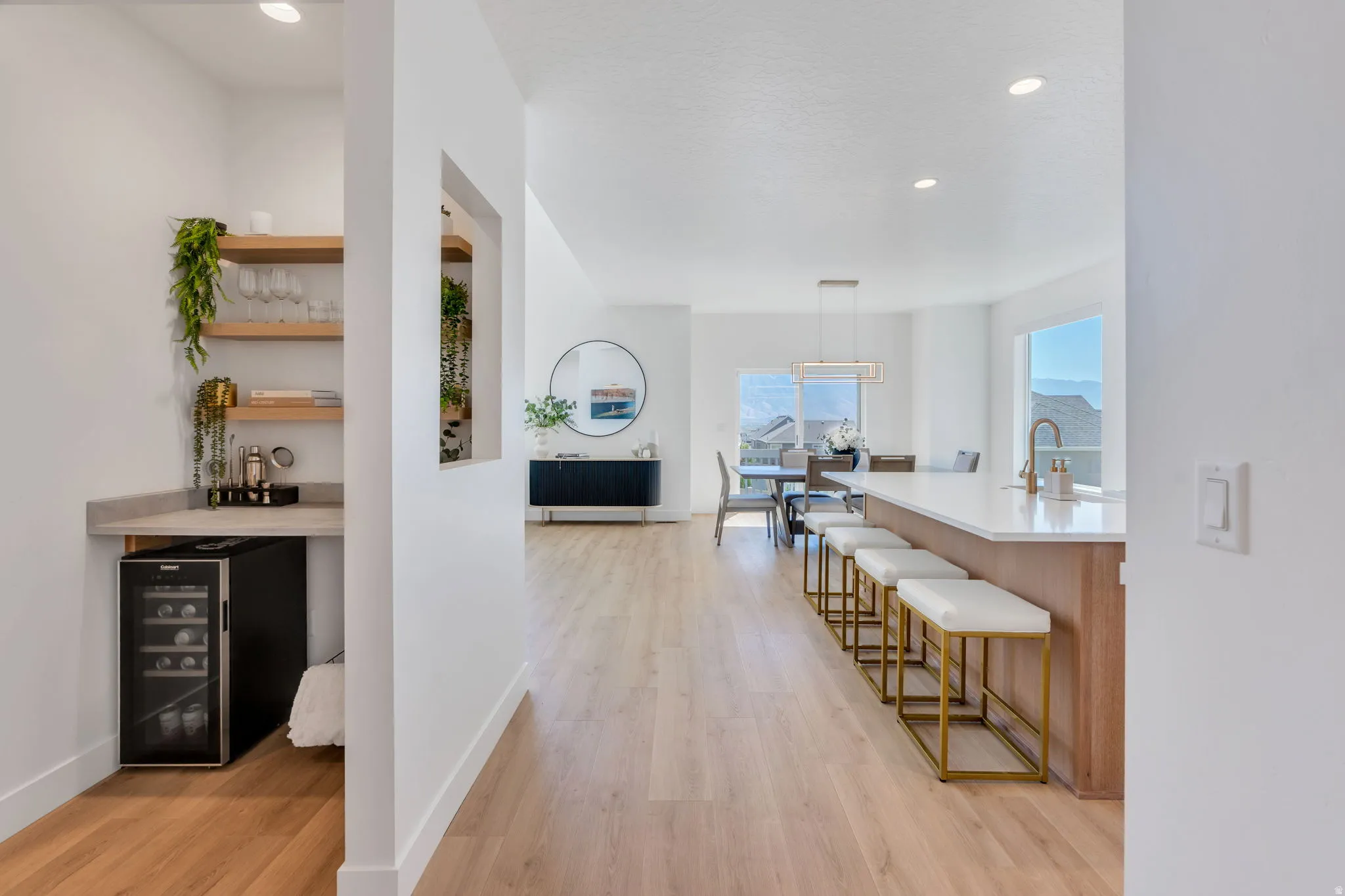 Open concept living area featuring light wood-finish flooring, a built-in wet bar with floating shelves and beverage refrigerator, a kitchen island with seating, and a dining area