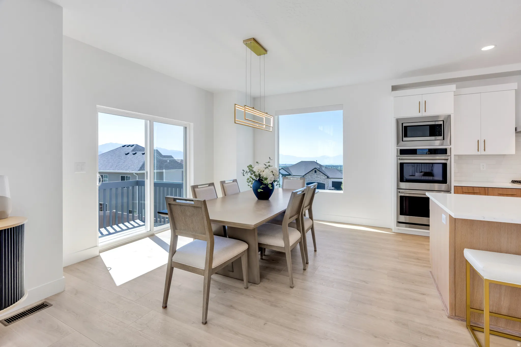 Open-concept dining area featuring light wood-finish flooring, a contemporary linear chandelier, and expansive windows