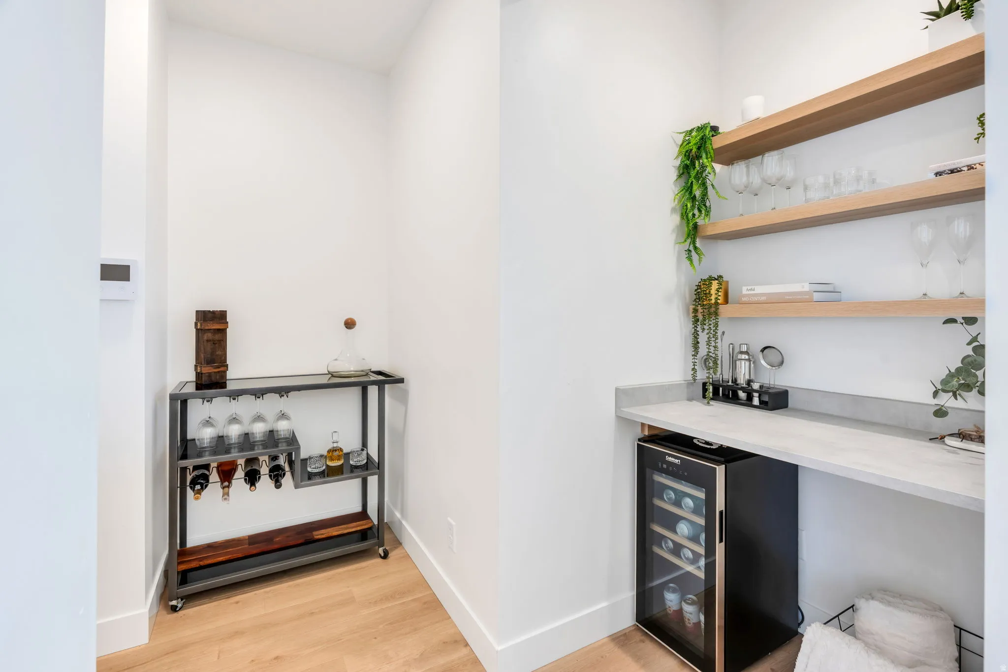 Built-in bar area featuring light wood-finish floating shelves, a light-toned countertop, and an under-counter beverage cooler