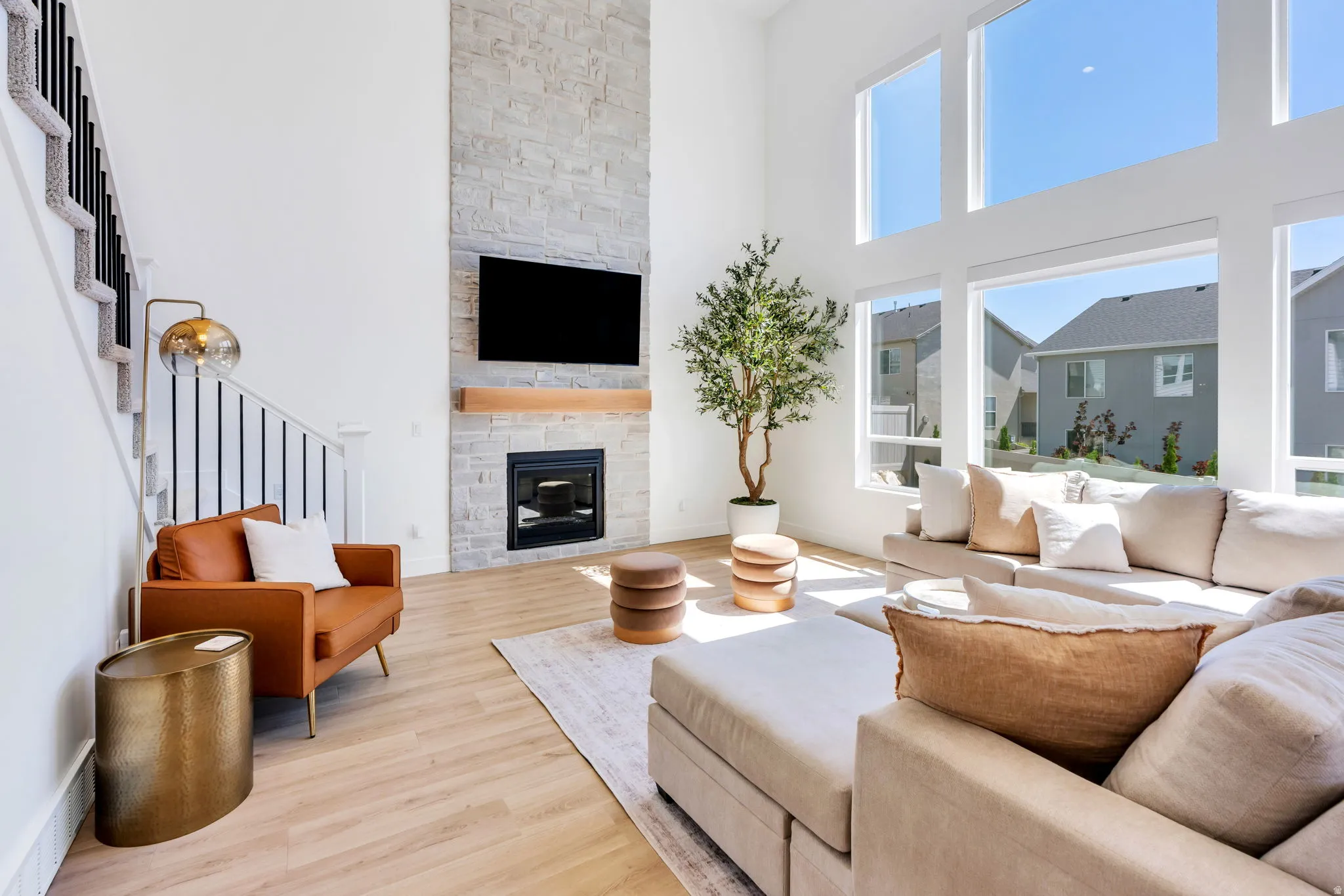Spacious living area featuring a floor-to-ceiling stone fireplace, high ceilings, large windows, wood-finish flooring, and a staircase with an open-rail design