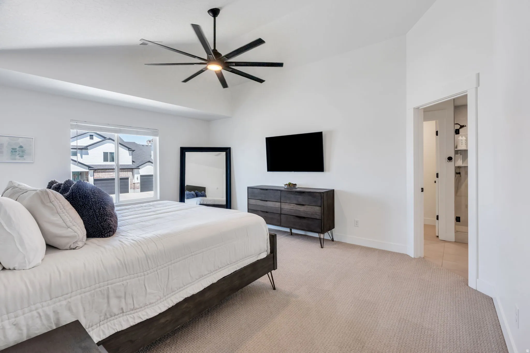 Spacious interior featuring a vaulted ceiling with a modern ceiling fan, neutral carpet flooring, and a large window