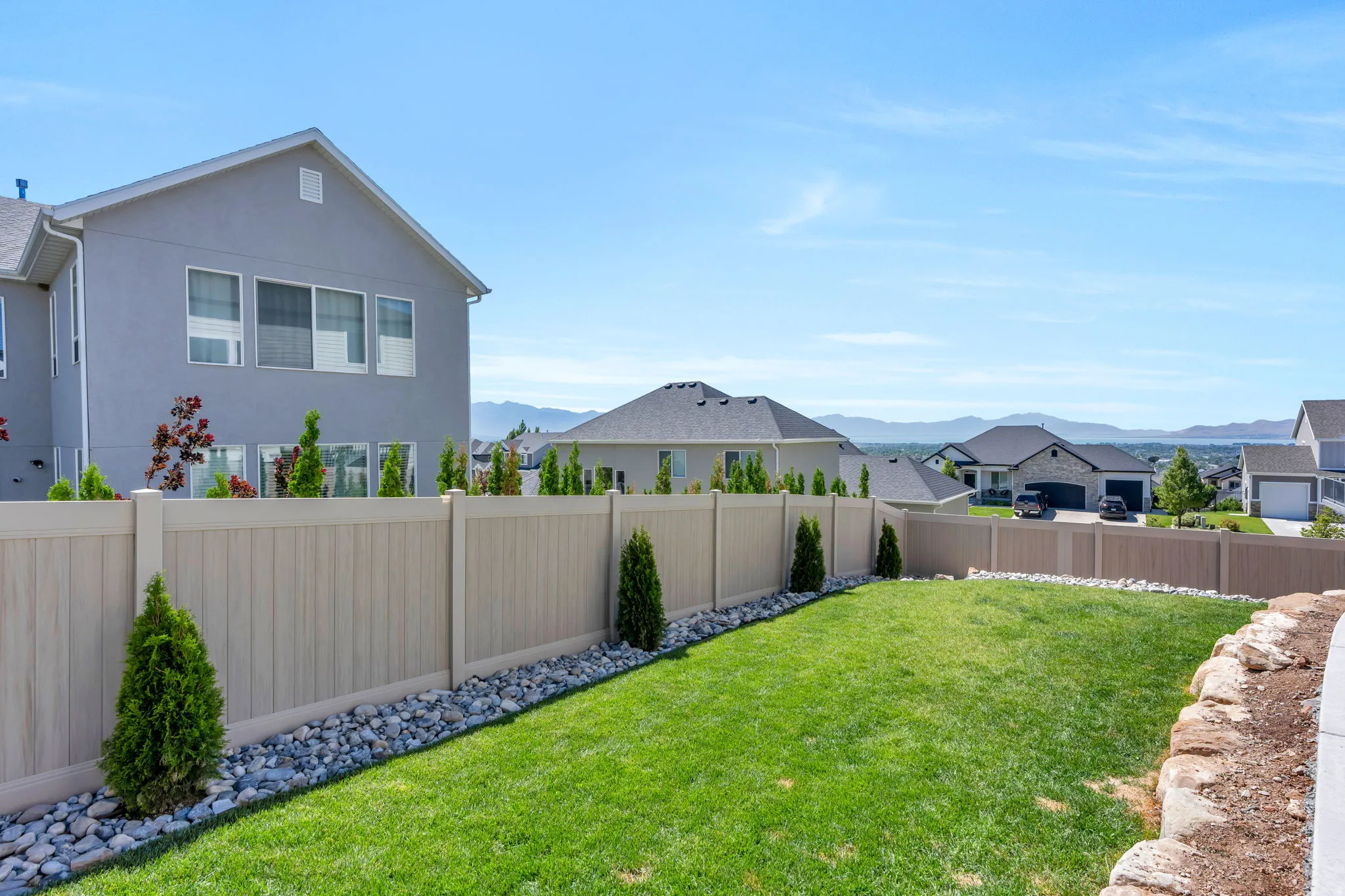 Expansive backyard featuring a manicured lawn, full fencing, decorative rock landscaping, and mature shrubbery