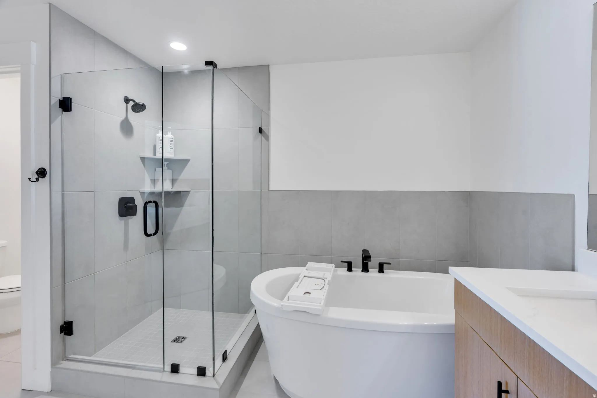 Modern bathroom featuring a freestanding soaking tub, a frameless glass shower enclosure with matte black fixtures, a built-in shower shelf, and light wood-finish vanity with a white countertop