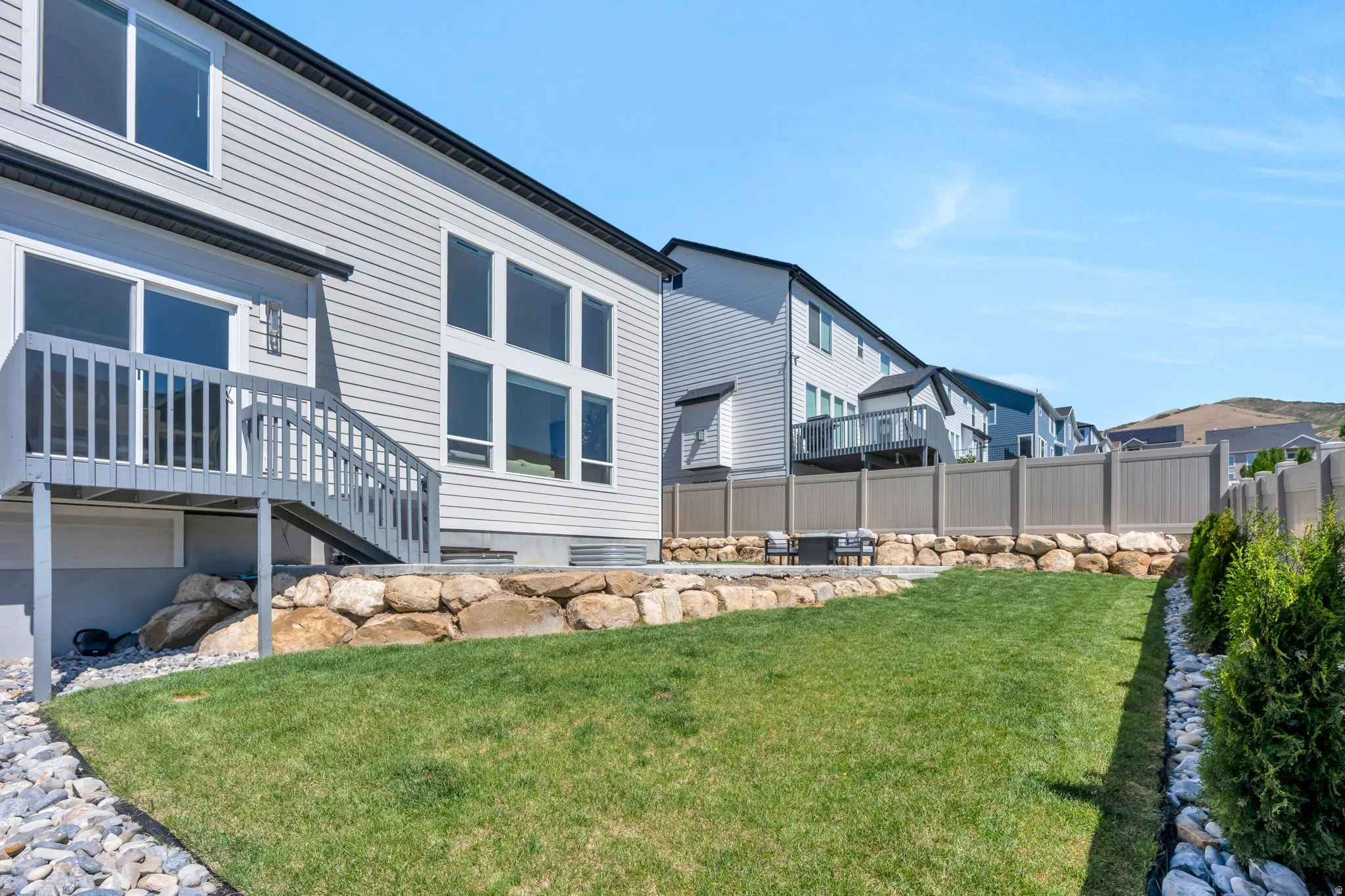 Expansive backyard featuring a manicured lawn, a stone retaining wall, and a concrete patio