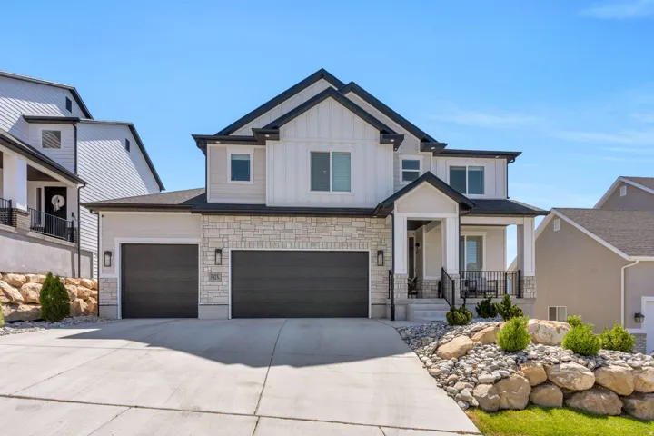 Modern two-story residence featuring a two-car garage, stone and siding exterior, covered porch, and well-maintained rock landscaping