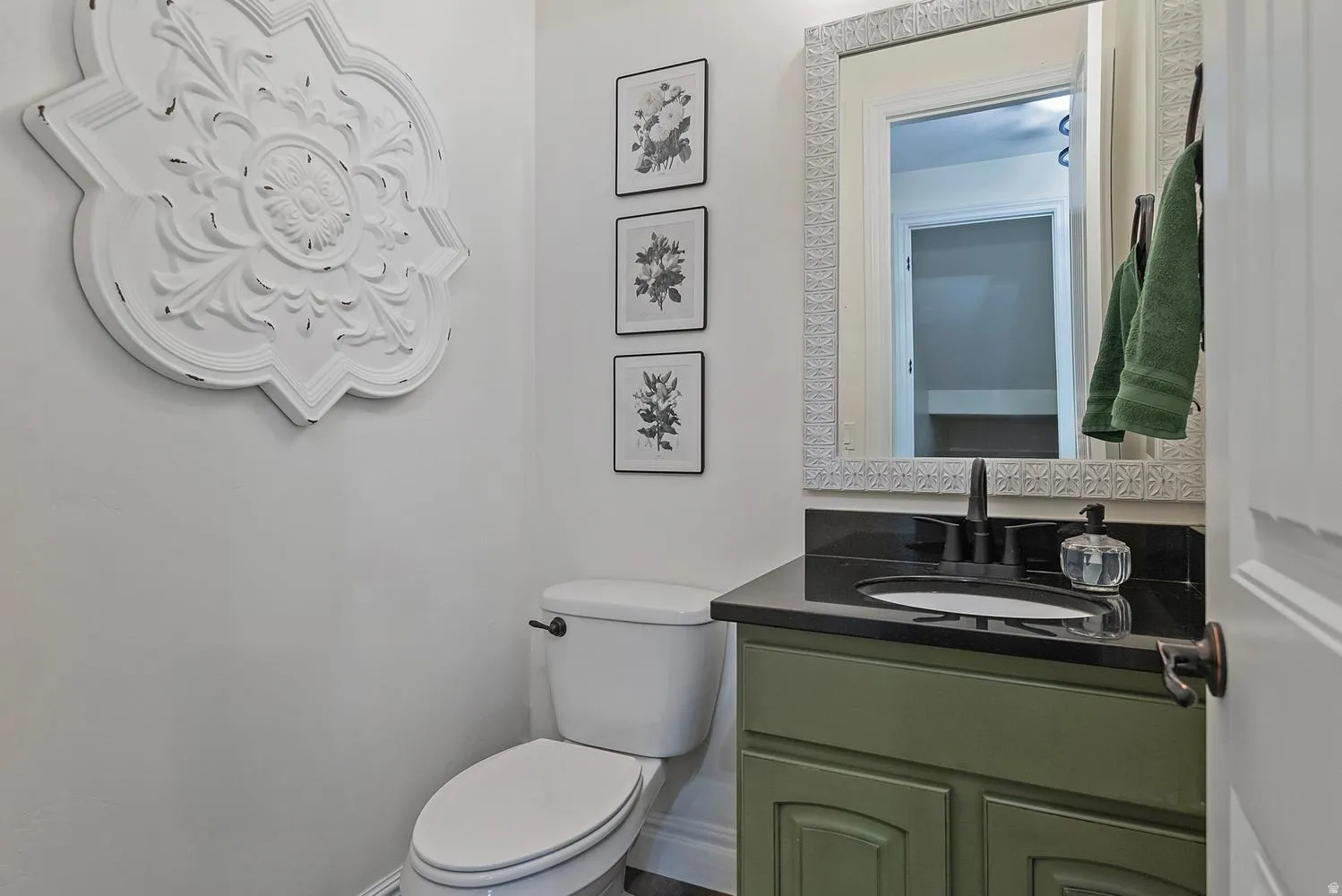 Bathroom featuring a green vanity with a black countertop, framed mirror, and white toilet