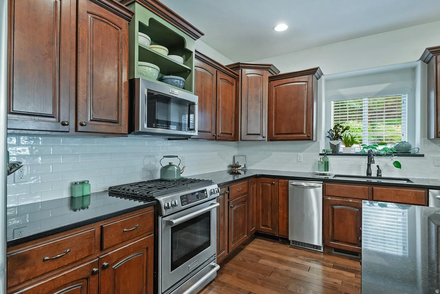 Kitchen featuring rich wood cabinetry, dark countertops, a white subway tile backsplash, stainless steel appliances, and wood-finish flooring