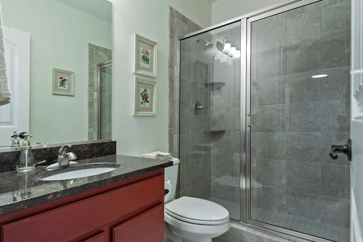 Bathroom featuring a red wood-finish vanity, dark speckled countertop, and an undermount sink with a chrome faucet