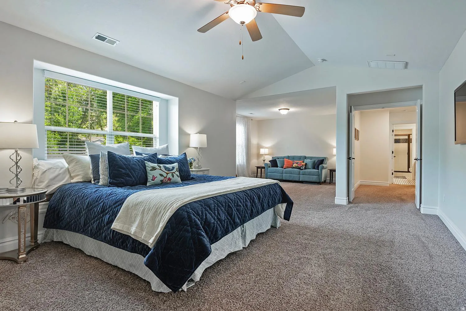 Expansive carpeted room featuring a large window, a ceiling fan with integrated lighting, and vaulted ceilings